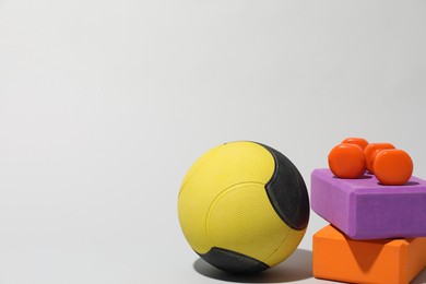 Photo of Medicine ball, dumbbells and foam blocks on light grey background, space for text