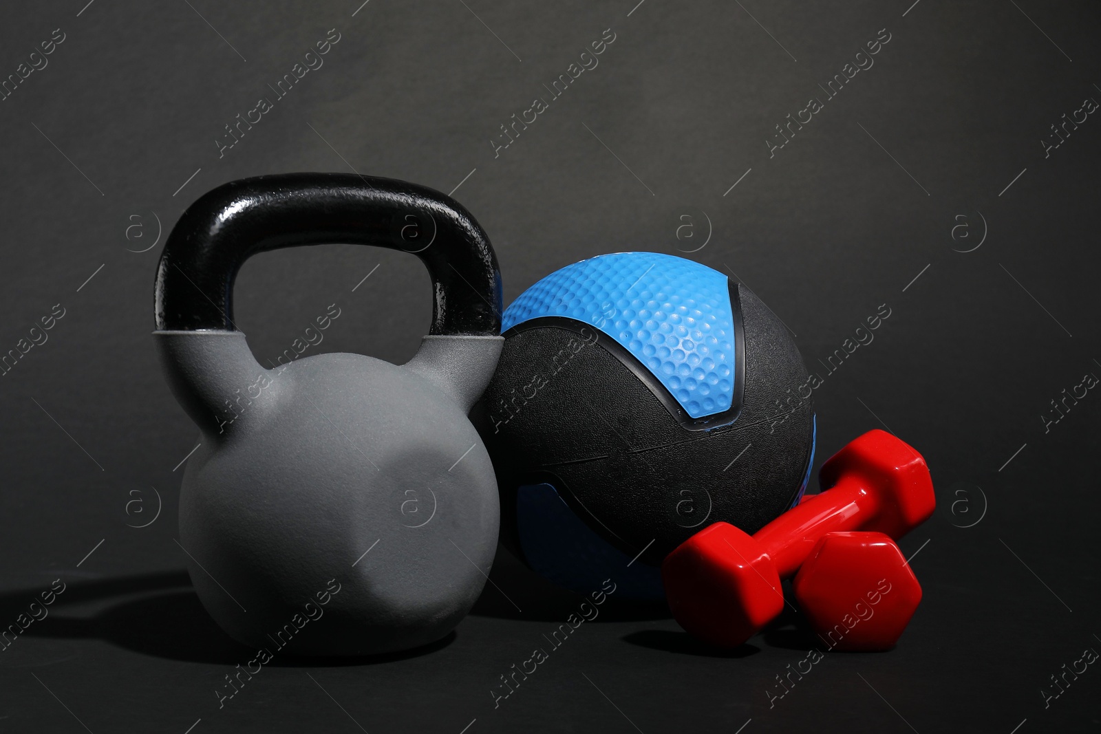Photo of Medicine ball, dumbbells and kettlebell on black background