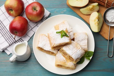 Photo of Pieces of tasty apple strudel with powdered sugar, mint and fruits on light blue wooden table, flat lay