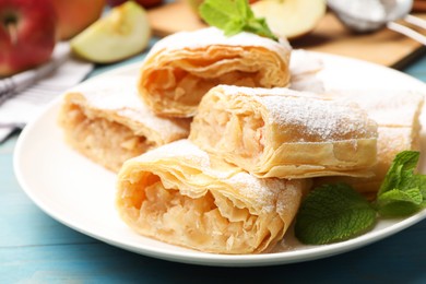 Photo of Pieces of tasty apple strudel with powdered sugar and mint on light blue wooden table, closeup