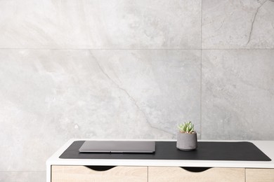Photo of Stylish workplace with laptop and black mousepad on white table indoors. Space for text