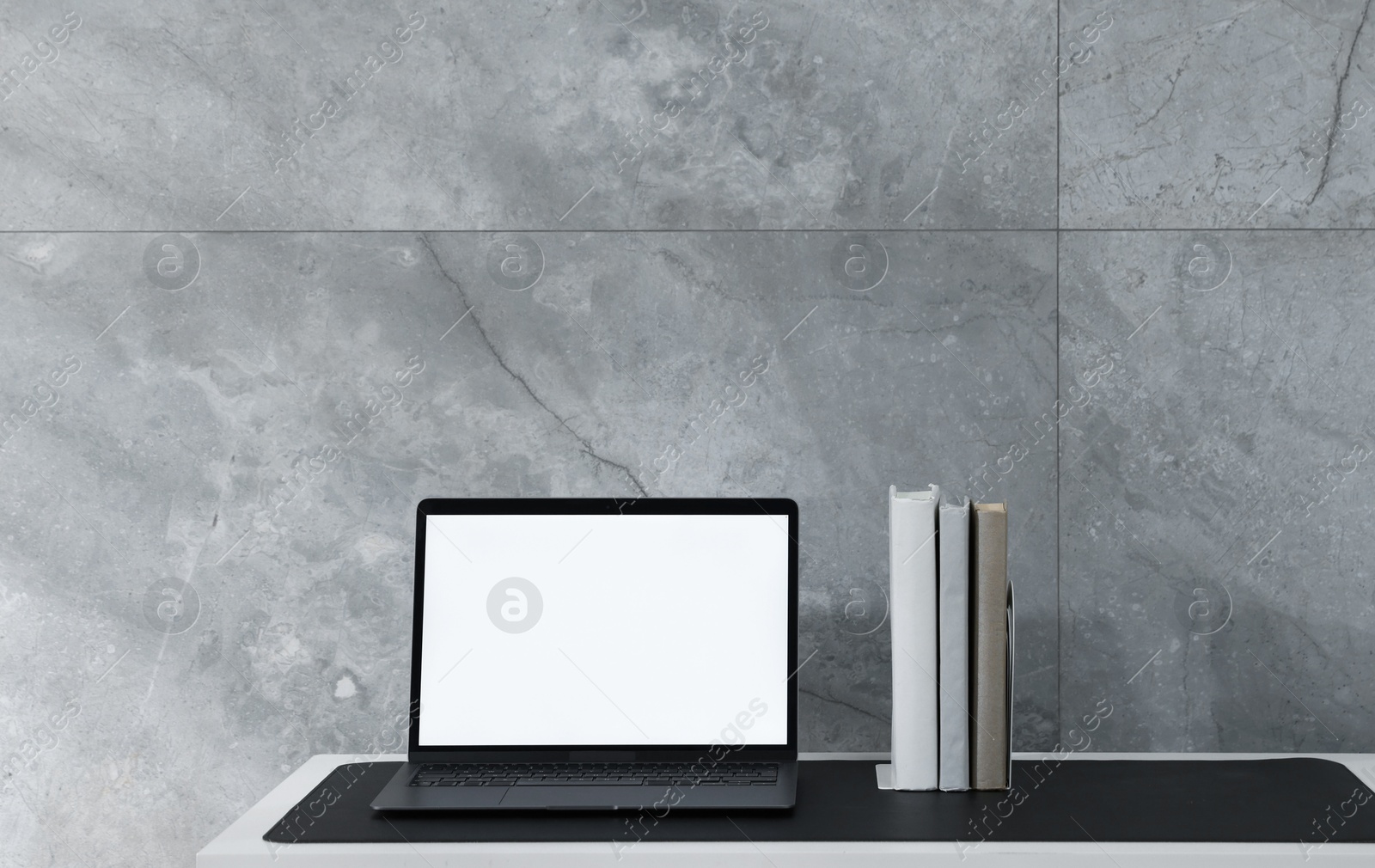 Photo of Stylish workplace with laptop and black mousepad on white table indoors. Space for text