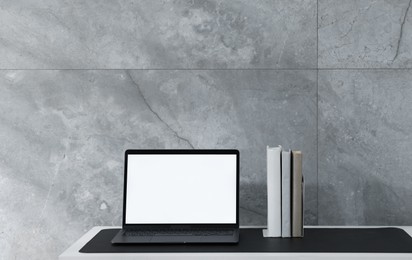 Photo of Stylish workplace with laptop and black mousepad on white table indoors. Space for text