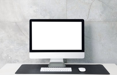 Photo of Stylish workplace with computer and black mousepad on white table indoors. Space for text