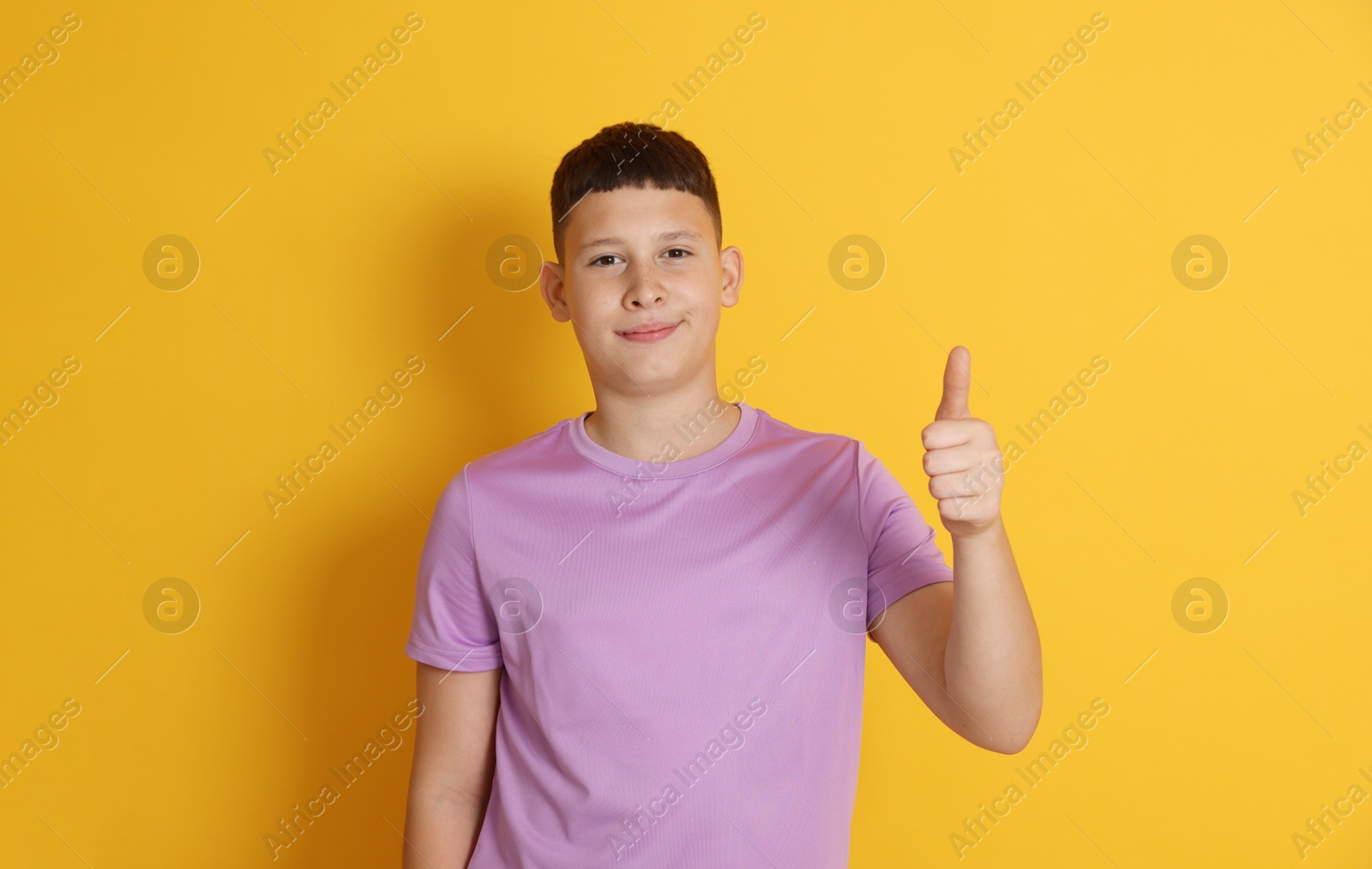 Teenage boy showing thumbs up on orange background Photo of Teenage boy showing thumbs up on orange background