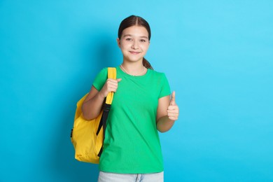 Photo of Teenage girl with backpack showing thumbs up on light blue background