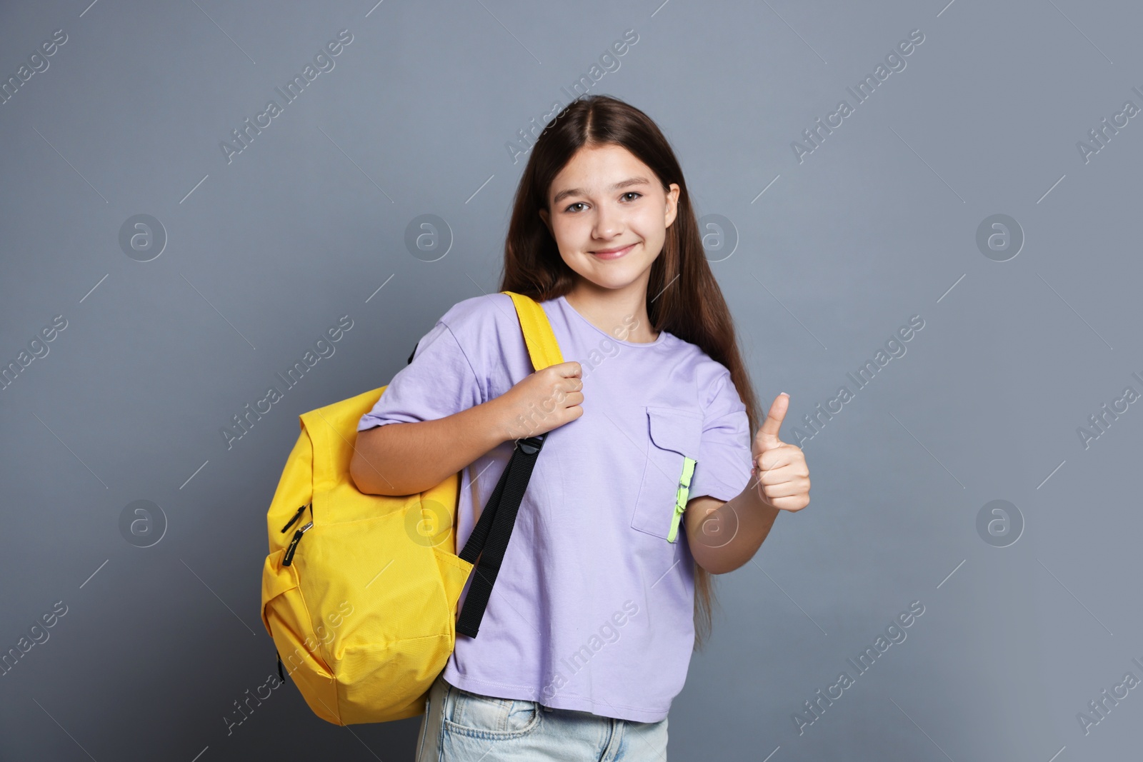 Teenage girl with backpack showing thumbs up on grey background Photo of Teenage girl with backpack showing thumbs up on grey background