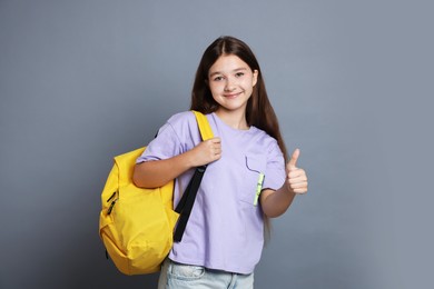Photo of Teenage girl with backpack showing thumbs up on grey background