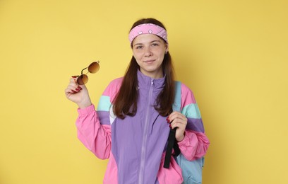 Photo of Teenage girl with sunglasses and backpack on yellow background