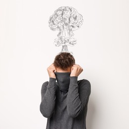 Image of Worried man covering his face. Confused thoughts depicted by explosion on white wall behind him. Stress, anxiety, depression