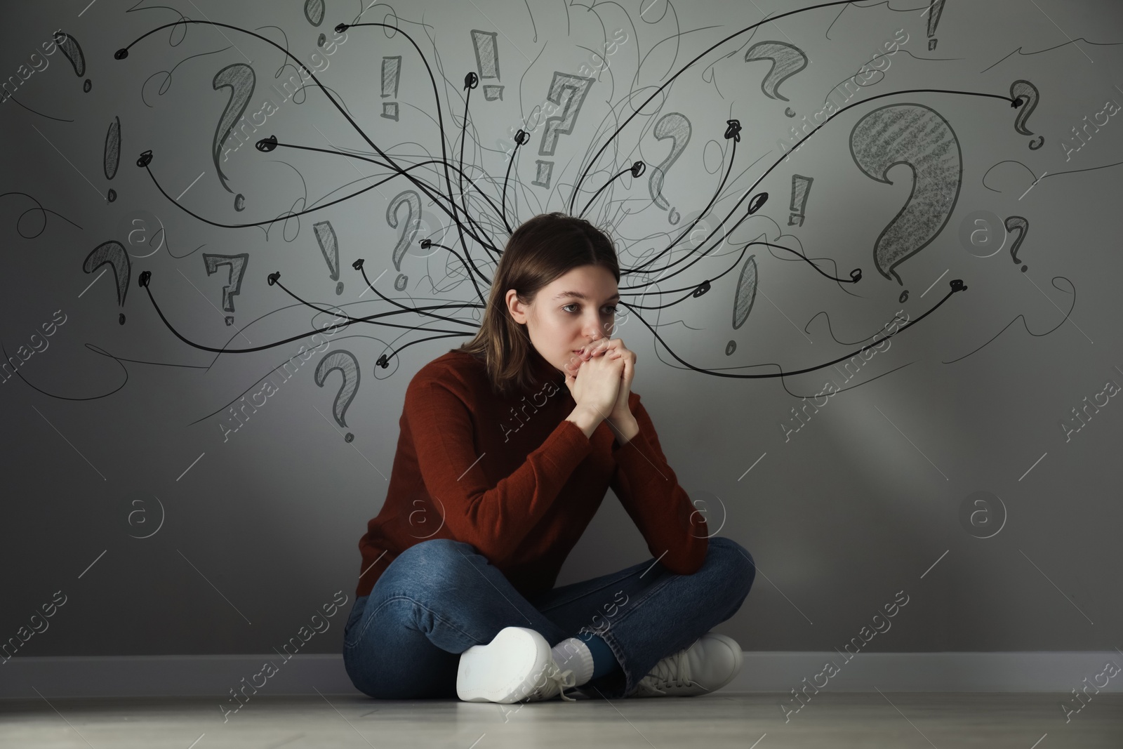 Worried woman sitting on floor. Confused thoughts depicted by arrows and lines on grey wall behind her. Stress, anxiety, depression Image of Worried woman sitting on floor. Confused thoughts depicted by arrows and lines on grey wall behind her. Stress, anxiety, depression