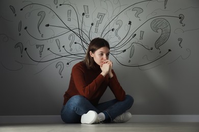 Image of Worried woman sitting on floor. Confused thoughts depicted by arrows and lines on grey wall behind her. Stress, anxiety, depression