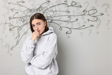 Image of Worried woman on grey background. Confused thoughts as doodles coming out of her head. Stress, anxiety, depression