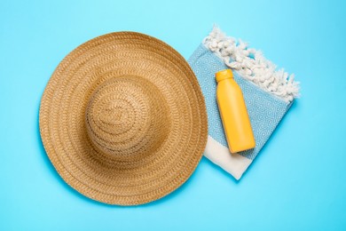 Photo of Straw hat, beach towel and sunscreen on light blue background, flat lay