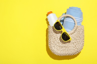 Photo of Wicker bag with beach towel and other summer accessories on yellow background, top view. Space for text