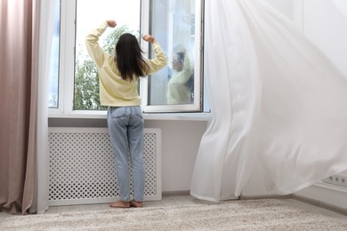 Photo of Harmony. Woman stretching near open window at home, back view