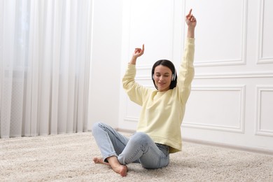 Photo of Harmony. Smiling woman in headphones enjoying music on floor near white wall at home