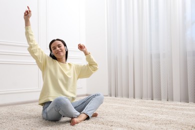 Photo of Harmony. Smiling woman in headphones enjoying music on floor near white wall at home. Space for text