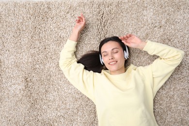 Photo of Harmony. Smiling woman in headphones enjoying music on beige carpet, top view. Space for text