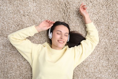 Photo of Harmony. Smiling woman in headphones enjoying music on beige carpet, top view