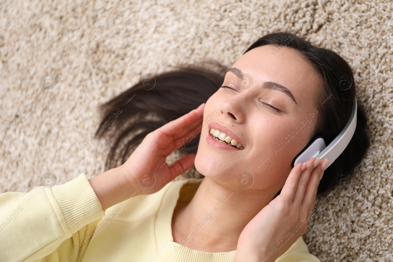 Harmony. Smiling woman in headphones enjoying music on beige carpet, closeup Photo of Harmony. Smiling woman in headphones enjoying music on beige carpet, closeup