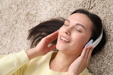 Photo of Harmony. Smiling woman in headphones enjoying music on beige carpet, closeup
