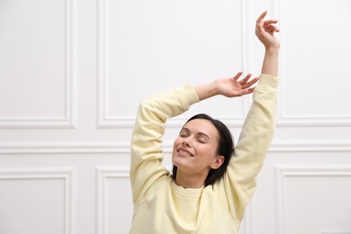 Photo of Harmony. Smiling woman stretching near white wall at home