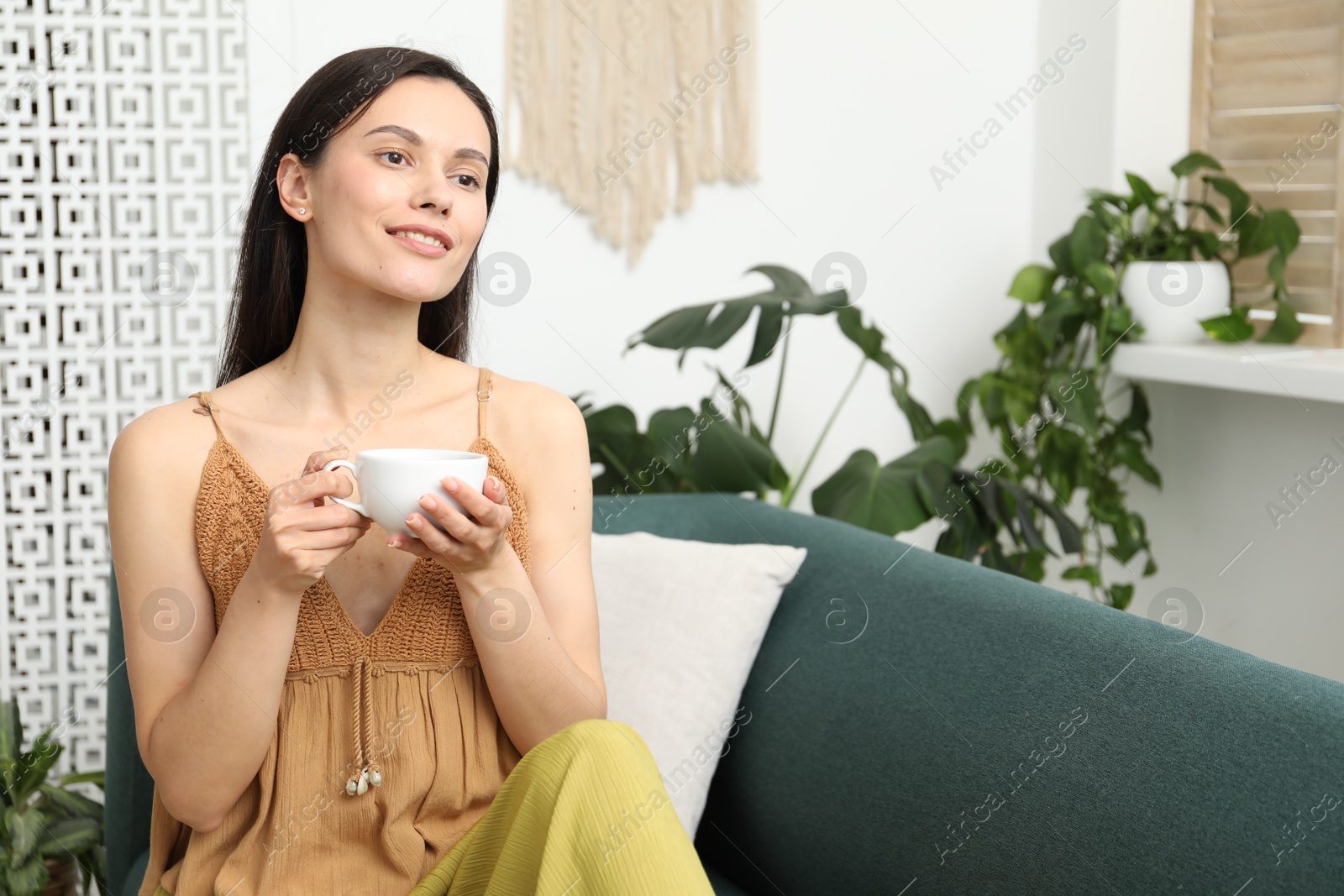 Harmony. Smiling woman with cup of hot drink relaxing on sofa at home Photo of Harmony. Smiling woman with cup of hot drink relaxing on sofa at home
