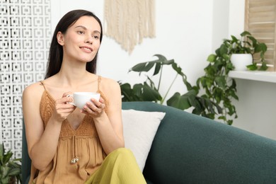 Photo of Harmony. Smiling woman with cup of hot drink relaxing on sofa at home