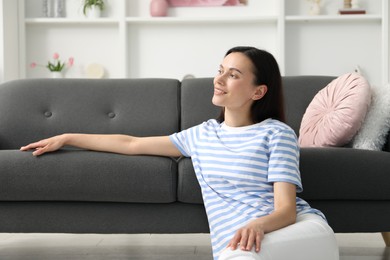 Photo of Harmony. Smiling woman relaxing while leaning on sofa at home