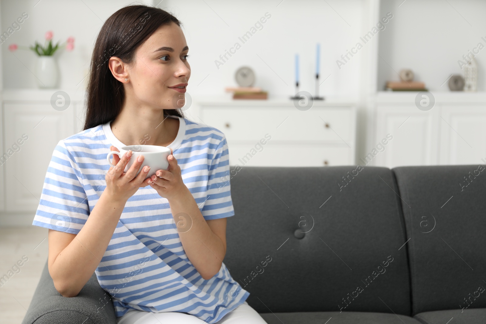 Harmony. Smiling woman with cup of hot drink relaxing on sofa at home, space for text Photo of Harmony. Smiling woman with cup of hot drink relaxing on sofa at home, space for text