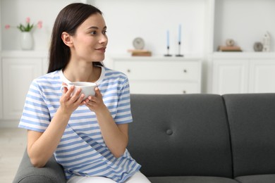 Photo of Harmony. Smiling woman with cup of hot drink relaxing on sofa at home, space for text