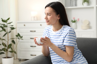 Photo of Harmony. Smiling woman with cup of hot drink relaxing on sofa at home, space for text