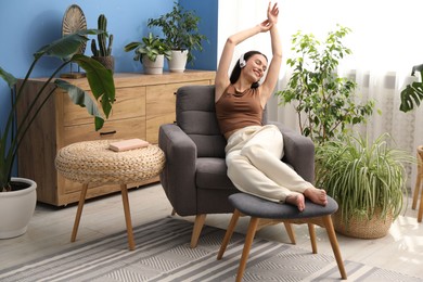 Photo of Harmony. Smiling woman in headphones relaxing on armchair among green plants at home