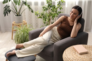Photo of Harmony. Smiling woman in headphones relaxing on armchair among green plants at home