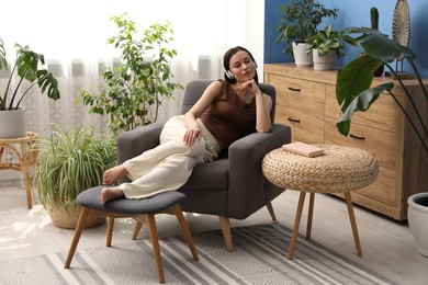 Photo of Harmony. Beautiful woman in headphones relaxing on armchair among green plants at home