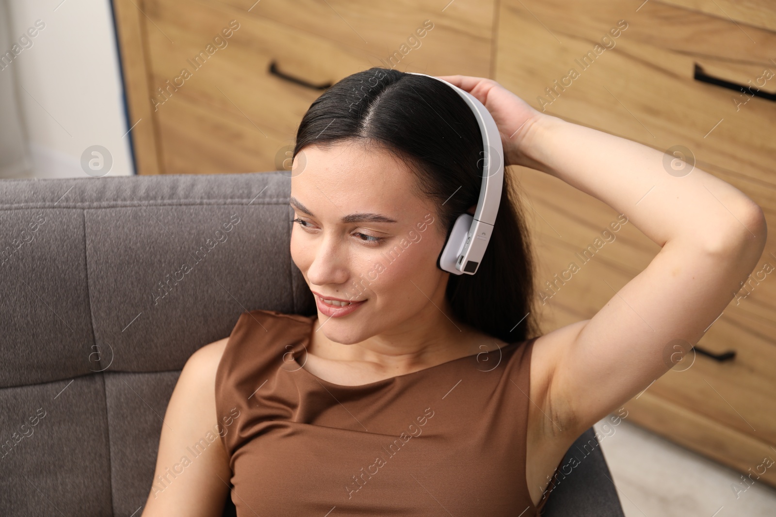 Harmony. Smiling woman in headphones enjoying music on armchair at home Photo of Harmony. Smiling woman in headphones enjoying music on armchair at home