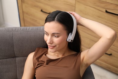 Photo of Harmony. Smiling woman in headphones enjoying music on armchair at home