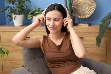 Photo of Harmony. Smiling woman in headphones enjoying music on armchair at home