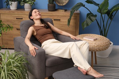 Photo of Harmony. Smiling woman relaxing on armchair among green plants at home