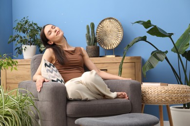 Photo of Harmony. Beautiful woman relaxing on armchair among green plants at home