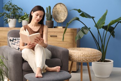 Photo of Harmony. Beautiful woman reading book on armchair among green plants at home