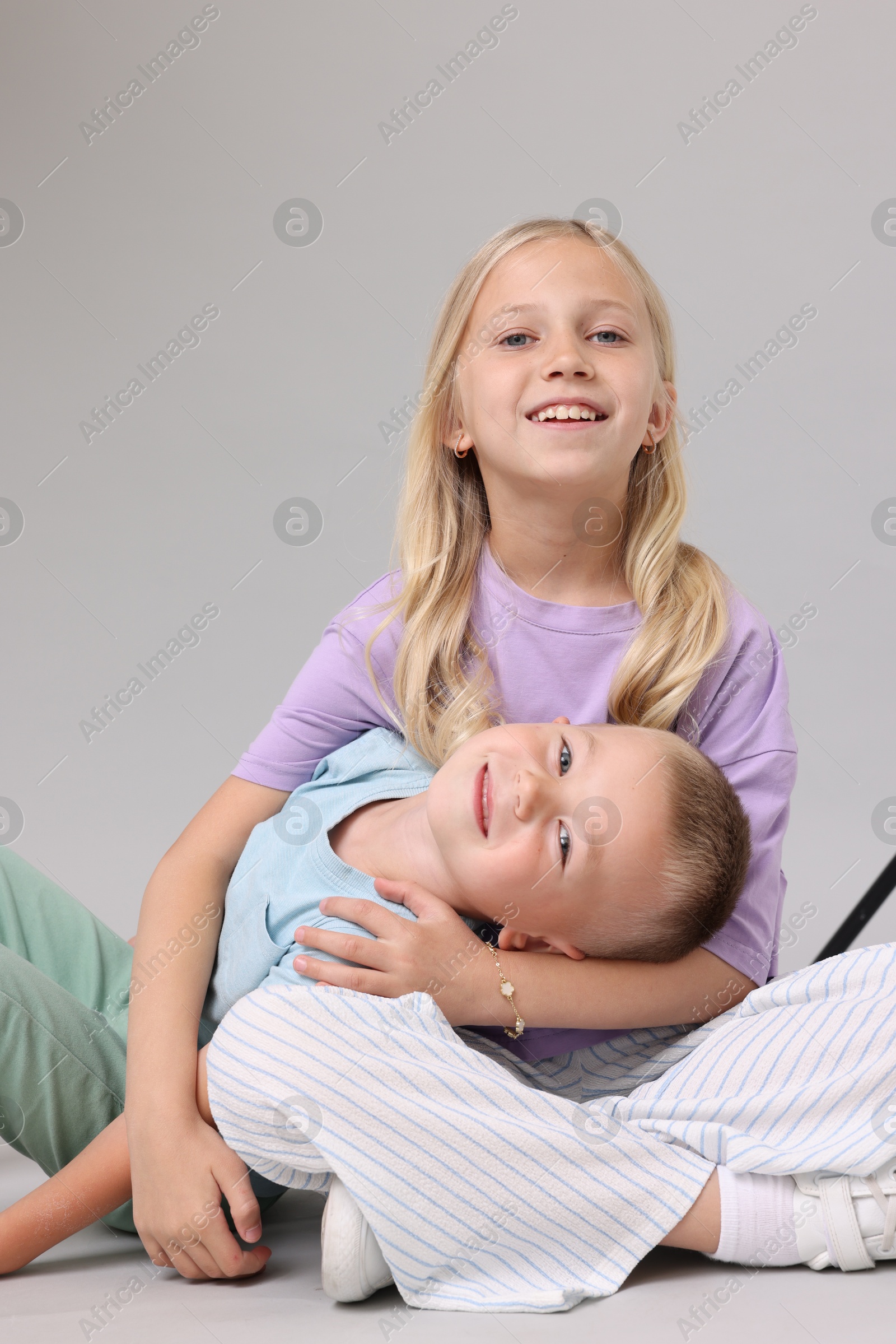 Little girl with her brother on light grey background in photo studio Photo of Little girl with her brother on light grey background in photo studio