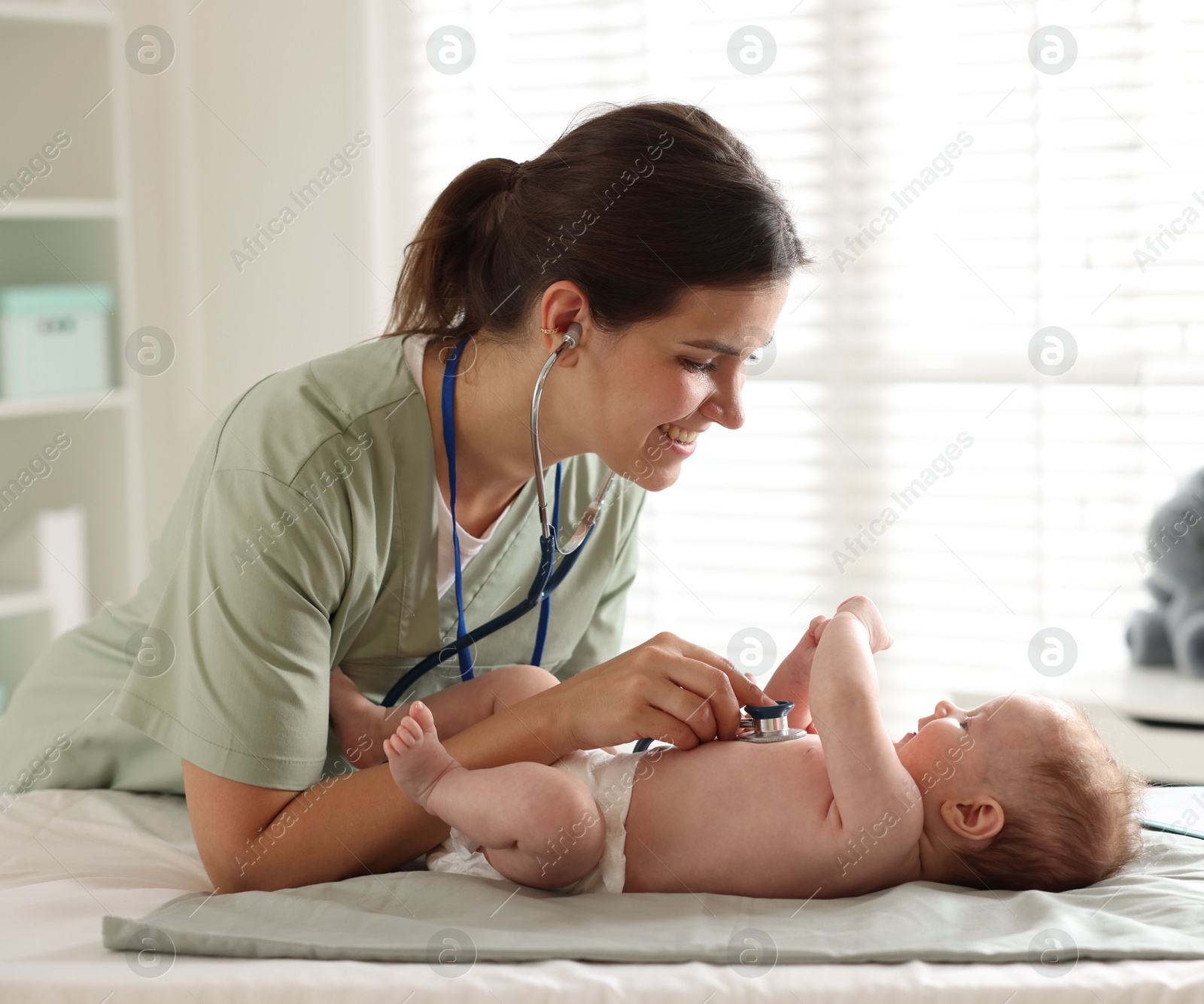 Photo of Mother and her cute little child having appointment with pediatrician in hospital. Doctor examining baby with stethoscope