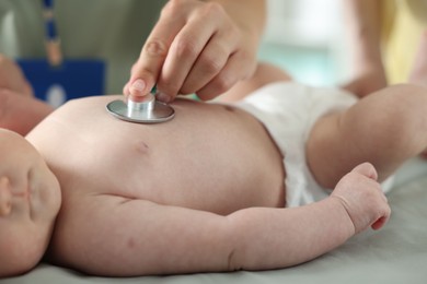 Photo of Mother and her cute little child having appointment with pediatrician in hospital. Doctor examining baby with stethoscope, closeup