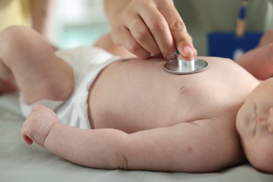 Photo of Mother and her cute little child having appointment with pediatrician in hospital. Doctor examining baby with stethoscope, closeup