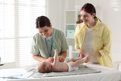 Photo of Mother and her cute little child having appointment with pediatrician in hospital. Doctor examining baby with stethoscope