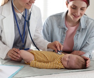 Photo of Mother and her cute little child having appointment with pediatrician in hospital. Doctor examining baby with stethoscope, closeup