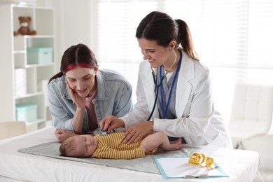 Photo of Mother and her cute little child having appointment with pediatrician in hospital. Doctor examining baby with stethoscope