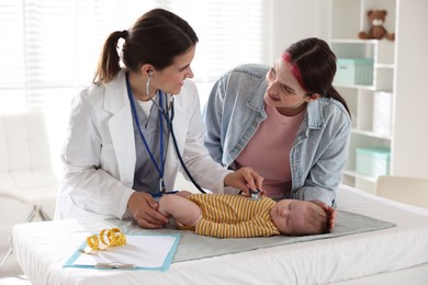 Photo of Mother and her cute little child having appointment with pediatrician in hospital. Doctor examining baby with stethoscope